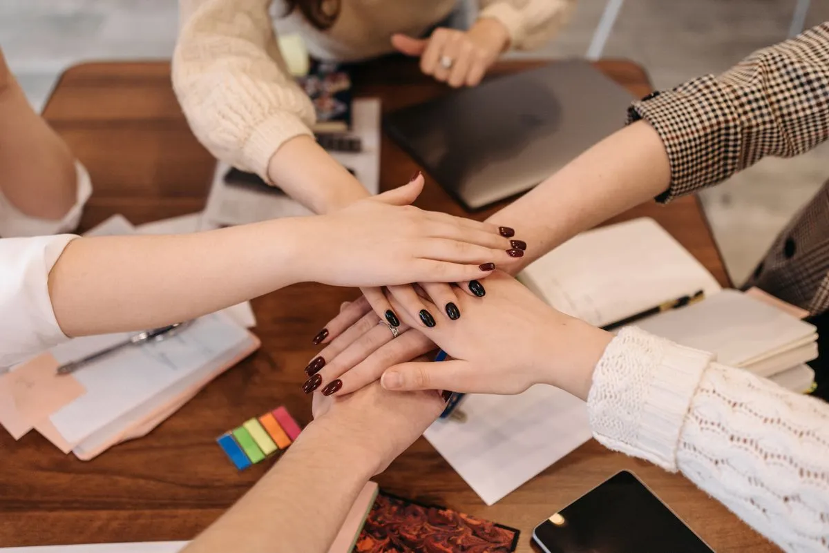 A team stacking their hands together over a desk of notebooks and a laptop